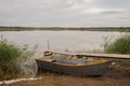 A gray boat stands on the shore of the lake next to a wooden bridge in cloudy weather Royalty Free Stock Photo