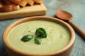 Wooden bowl of delicious broccoli cream soup with basil on table