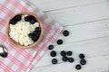 Wooden bowl of farmer cheese on red and white napkin and a pile of blueberry on white wooden background flat lay. Healthy eating