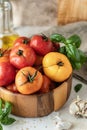 Wooden bowl of fresh colorful tomatoes, garlic, basil, pepper and olive oil on textured background. Kitchen still life in rustic Royalty Free Stock Photo