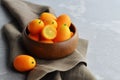 Wooden bowl full of fresh kumquat fruits on brown linen napkin on grey concrete background Royalty Free Stock Photo