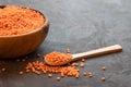 A wooden bowl full of raw red lentils and a wooden spoon filled with lentil grains next to a dark background. Place for text Royalty Free Stock Photo