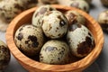 Wooden bowl and many speckled quail eggs on table, closeup