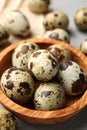 Wooden bowl and many speckled quail eggs on table, closeup