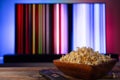 A wooden bowl of popcorn and remote control in the background the TV works. Evening cozy watching a movie or TV series Royalty Free Stock Photo