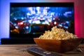 A wooden bowl of popcorn and remote control in the background the TV works. Evening cozy watching a movie or TV series Royalty Free Stock Photo