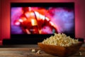 A wooden bowl of popcorn and remote control in the background the TV works. Evening cozy watching a movie or TV series Royalty Free Stock Photo