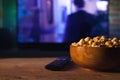 A wooden bowl of popcorn and remote control in the background the TV works. Evening cozy watching a movie or TV series at home Royalty Free Stock Photo