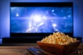 A wooden bowl of popcorn and remote control in the background the TV works. Evening cozy watching a movie or TV series Royalty Free Stock Photo