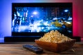 A wooden bowl of popcorn and remote control in the background the TV works. Evening cozy watching a movie or TV series Royalty Free Stock Photo