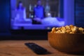 A wooden bowl of popcorn and remote control in the background the TV works. Evening cozy watching a movie or TV series at home