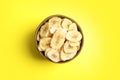 Wooden bowl with sweet banana slices on color background, top view. Dried fruit