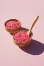 Wooden bowls with a spoon filled with pink bath sea salt. Beauty treatment for spa and wellness on pink background. Royalty Free Stock Photo