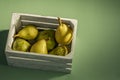 Wooden box full of ripe pears of different varieties on plain green background Royalty Free Stock Photo