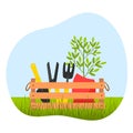 A wooden box with garden tools, pruning shears, a shovel and a ripper, and a planter with a home flower on the