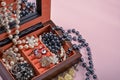 A wooden box with a mirror filled with rings and pearl beads and earrings close up on a beige background. Photo stylized as an oil