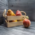 A wooden box with rope handles is filled with ripe red and yellow pears