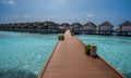 A wooden bridge leading to the houses on stilts above sea level. There are flowers on the bridge Royalty Free Stock Photo