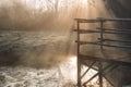 Wooden bridge over lake in early misty morning, fog over the water on sun rays Royalty Free Stock Photo