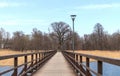 A wooden bridge with a light pole on it and a large tree at the end of the bridge Royalty Free Stock Photo