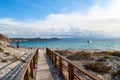 A wooden bridge leads to a sandy beach on the island of Sardinia in Italy. Beautiful sea with a small boat in the Costa Smeralda. Royalty Free Stock Photo