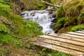 Wooden bridge with small waterfall surrounded by lush green vegetation in Gjain Canyon in Thjorsardalur valley, Iceland Royalty Free Stock Photo