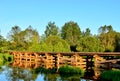 A wooden bridge of tree logs lies across a small river inside a wooded area among green nature. Royalty Free Stock Photo