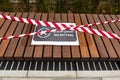 Wooden brown bench with `No Sitting` sign in english and arabic and red and white barricade tape, COVID-19 in Dubai Royalty Free Stock Photo