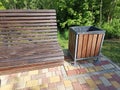 A wooden brown bench for relaxing in a city park, next to it is a trash can. Walking path for outdoor walks Royalty Free Stock Photo