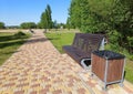 A wooden brown bench for relaxing in a city park, next to it is a trash can. Walking path for outdoor walks Royalty Free Stock Photo