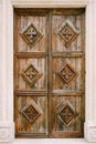 A wooden brown door with carved diamonds and patterns in the opening of a white wall.