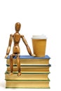 Wooden brown mannequin sits stack of books, next to glass of coffee.Concept reading books.