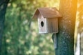 Wooden brown new bird house or nesting box attached to tree trunk in summer park or forest on blurred sunny green foliage bokeh Royalty Free Stock Photo