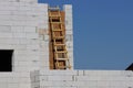 Wooden brown staircase by the gray brick wall of an unfinished house against the blue sky Royalty Free Stock Photo