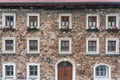 A wooden, brown windows and a fragment of a stone wall of the building. Curtains hanging in the window, colorful flowers Royalty Free Stock Photo