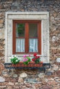 A wooden, brown window and a fragment of a stone wall of the building. Curtains hanging in the window, colorful flowers Royalty Free Stock Photo