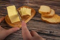 Wooden butter dish with a piece of butter and slices of cheese and fresh wheat toast on a wooden background. Someone cuts off a