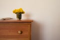 Wooden cabinet with vase of yellow flowers and piece of white material. Royalty Free Stock Photo