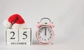 Wooden calendar December 25 covered with red santa christmas hat with pink vintage alarm clock show 12 o`clock  on white Royalty Free Stock Photo