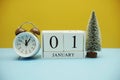 Wooden calendar 1st January with alarm clock and chirtsmas tree on yellow and blue background Royalty Free Stock Photo