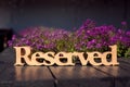 Wooden carved reserved table sign , pink flowers background, wooden table in outdoor restaurant Royalty Free Stock Photo