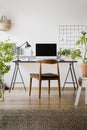 Wooden chair at desk with lamp and computer desktop in home office interior with plants. Real photo Royalty Free Stock Photo