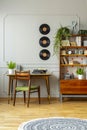 Wooden chair at desk with plant in vintage workspace interior with vinyl, cabinet and rug. Real photo Royalty Free Stock Photo