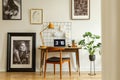 Wooden chair at desk with yellow lamp and laptop in home office interior with gallery. Real photo