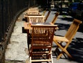 Wooden chairs, restaurant tables and terrace along old rusty wrought iron fence on street in bright light Royalty Free Stock Photo