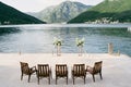 Wooden chairs stand in a row in front of a wedding semi-arch on a pier by the sea