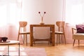 Wooden chairs at table with flowers in bright living room interior with armchair. Real photo