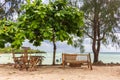 Wooden chairs and table under trees on tropical beach. Outdoor cafe furniture in resort garden against seascape.