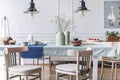 Wooden chairs at table in white cottage dining room interior with lamps and poster. Real photo