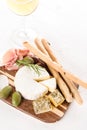 Wooden charcuterie board with selection of cheeses and prosciutto served with olives, grissini and glass of wine Royalty Free Stock Photo